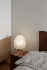 A minimalist bedroom with a wooden nightstand featuring a round lamp with a white shade, positioned next to a bed adorned wit