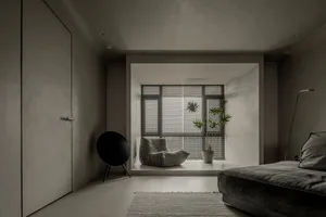 A minimalist living room with concrete walls and a sofa, a window with blinds, and a speaker.