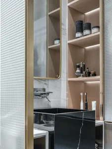 A modern bathroom with a square black sink, a frosted glass door, and a shelf with toiletries and a razor.