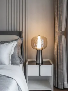 A modern bedroom featuring a glass table lamp and gray bedding with metallic accent.