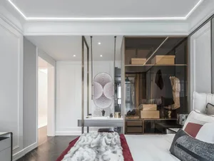 A modern bedroom featuring a bed with a fur blanket, white and burgundy pillows, and a metal-framed glass closet.