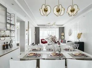 Modern dining room with gold and white decor, white table, red accent chairs, crystal chandelier, and metallic accents.