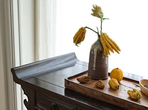 A stylish wooden concrete vase on a wooden surface with decorative fruits and a window in the background.