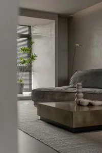 A modern living room with a minimalist design featuring a concrete coffee table and a gray couch with a vase of plants.