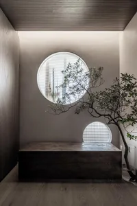 A modern living space featuring a wooden sofa with water droplets on it, set against a wall with two circular windows and a w
