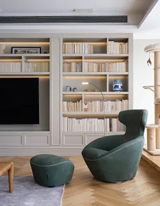 A modern minimalist living room with a green armchair, ottoman, and built-in bookshelves.