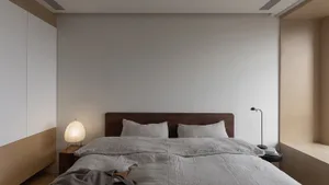 A minimalist bedroom with a bed, nightstand, and lamp, featuring neutral-toned bedding and decor.