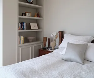 A minimalist bedroom featuring wood accents, fabric bedding, and glass vases, with a bedside table and bookshelf.