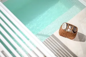 A wicker cane basket filled with rolled-up white towels placed beside a mint green swimming pool.