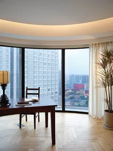 A modern home office with wooden furniture, glass windows, and a view of the city.