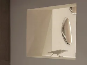 A small ceramic bird figurine sitting in a recessed shelf with reflective metallic plates nearby.
