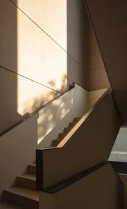 Modern staircase with concrete steps, wooden handrails, and sunlight casting patterns on the wall.