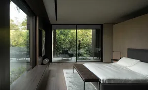 A modern bedroom featuring a comfortable bed with white linens, a minimalist design, and a large glass door providing a view 