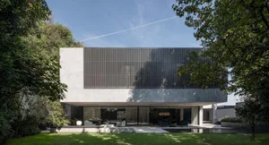 A modern house with a concrete exterior surrounded by greenery on a sunny day.