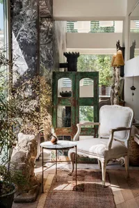 A vintage-inspired living room with a white armchair, a side table with a marble top, a green antique door, and various decor