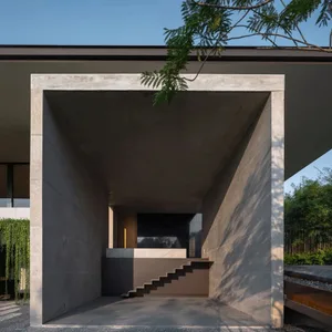 Concrete entrance lobby with stairs and greenery in the background.
