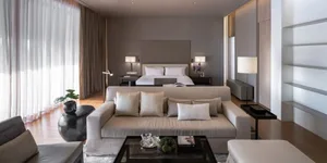 Neatly arranged modern living space featuring a large beige sofa with numerous white throw pillows, a glass coffee table ador