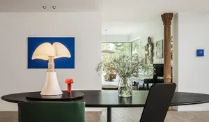 A modern dining room featuring a black oval table, white table lamp, and glass vase with dried flowers.