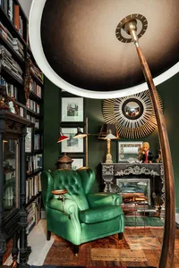 A modern home library featuring a green armchair, hardwood floors, and a large bookshelf filled with books.