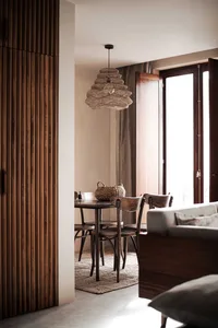 A minimalist dining room with wooden furniture, a wicker pendant light, and a fabric sofa.