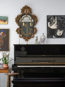 A black piano adorned with a framed mirror and sculptures, accompanied by framed artworks on the wall.