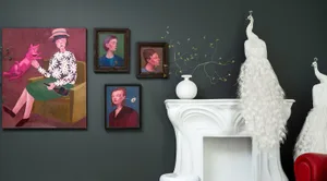 A collection of framed artworks and white peacocks on a mantel against a dark gray wall.