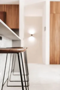 A modern minimalist kitchen with wooden accents, concrete countertops, and black metal stools.