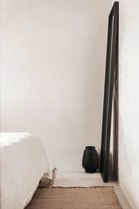 A minimalist bedroom featuring a concrete floor with a bed, vase, and mirror in a sleek, modern design.