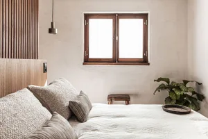 A minimalist bedroom with a wooden window, soft fabric bedding, and a small potted plant.