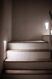 Modern staircase with tile steps and walls, illuminated by wall sconces.