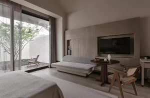 A minimalist bedroom with neutral-toned furniture and a large window overlooking greenery.