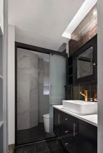 Modern bathroom interior with marble and black tile walls and floor, featuring a sink with a white countertop and black cabin