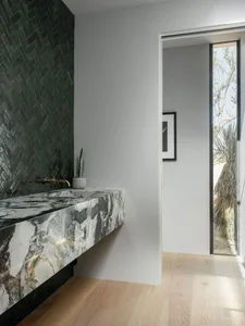 A modern bathroom with a marble countertop and black tiled walls.