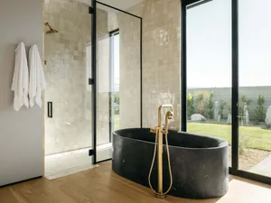 Modern bathroom with a freestanding black marble tub, glass shower enclosure, and white towels hanging on the wall.
