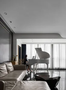 A modern living room with gray tiles, white curtains, and a leather couch featuring a grand piano.