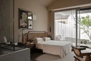 Modern minimalist bedroom featuring a natural fiber bedframe, white bedding, and a collection of framed artworks on the wall.