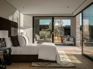 Modern minimalist bedroom with concrete walls and floor, glass sliding doors to an outdoor patio with desert landscaping.