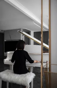A woman wearing a black dress playing a white piano in a sleek, modern room.