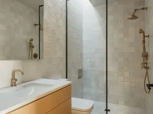 A modern bathroom with white and beige square tiles, a white sink, and a walk-in shower with glass doors.