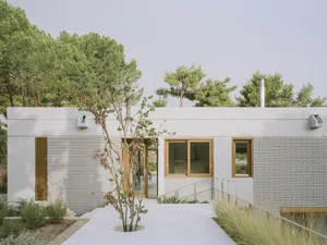 A modern house with white brick walls and large windows surrounded by greenery.