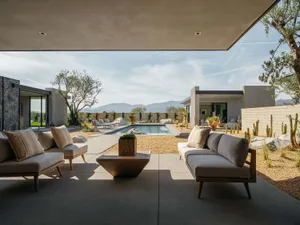 A modern outdoor living space featuring concrete and stone surfaces with a glass-walled patio area and landscaping.