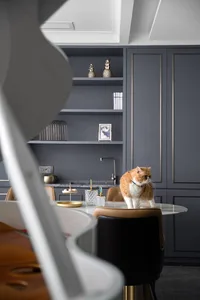 Modern kitchen with white cabinets, marble countertops, glass shelves, and a cat sitting on a marble table.