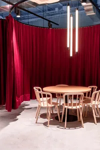 A conference room with a round wooden table and chairs, surrounded by red curtains and modern lighting.