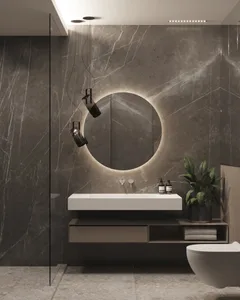 Modern bathroom with marble walls and floor, round mirror with backlit lighting, floating vanity, and green plant.