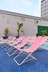 A row of pink foldable outdoor chairs arranged neatly in a poolside area with plants and a blue textured surface.