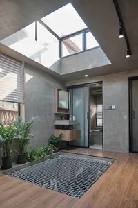 A modern industrial bathroom with concrete walls, a large skylight, and a grid floor.