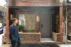 A modern storefront made of brick with a single black door, surrounded by green plants and windows.