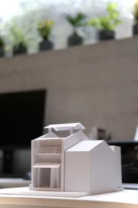 A small, white geometric model of a modern interior space made of paper.