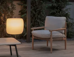 A minimalist outdoor furniture setup featuring a wooden chair with woven armrests and cushions, accompanied by a round, illum
