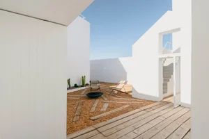 Minimalist outdoor terrace featuring wooden deck, gravel flooring, and glass walls.